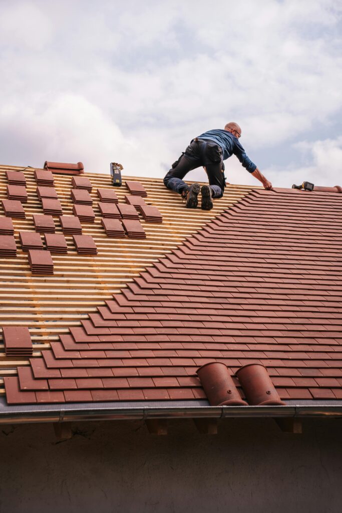 A roofer carefully installs shingles on a new residential roof under a cloudy sky.